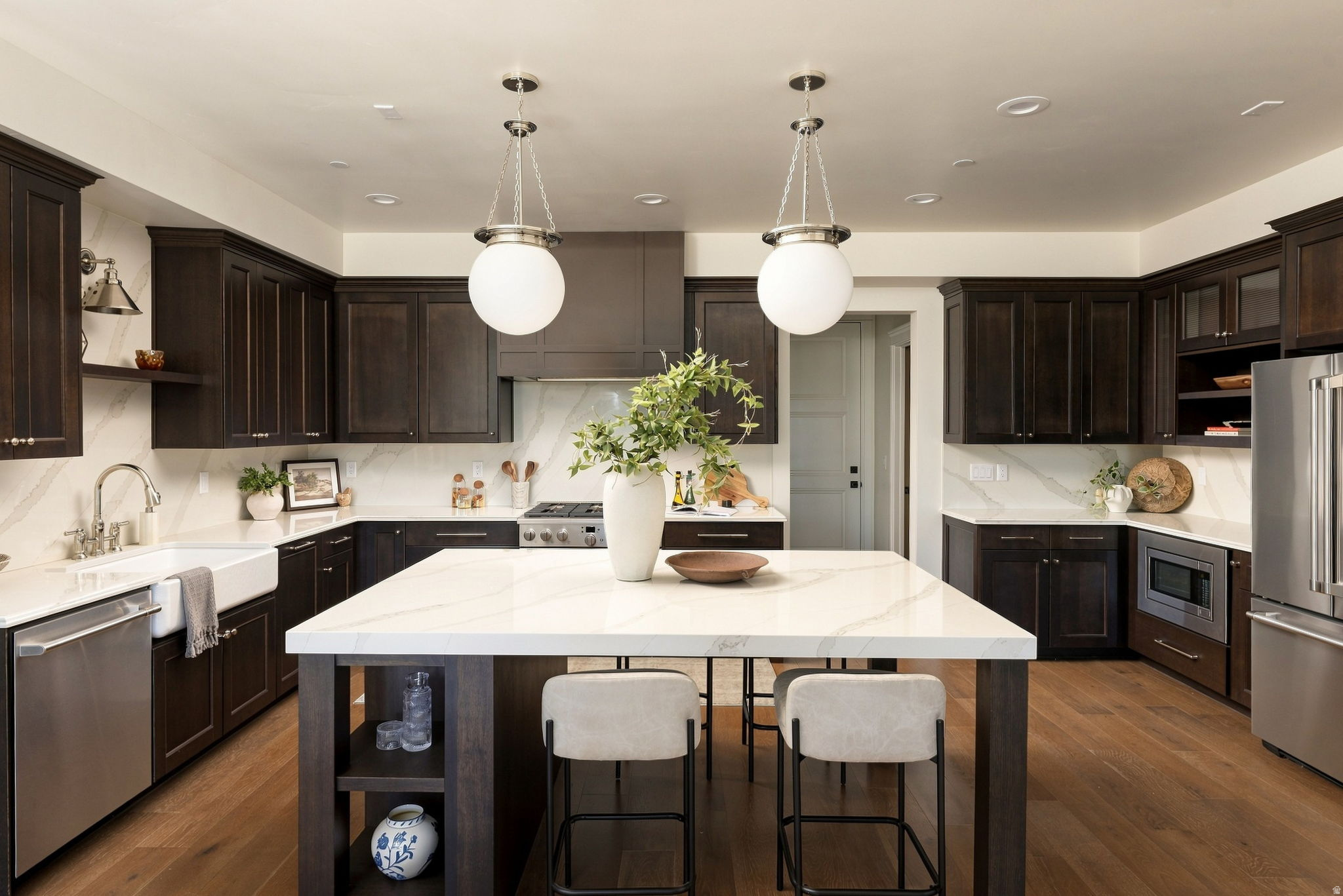 Expansive kitchen featuring wood-finish flooring, dark wood cabinetry, white stone countertops, and stainless steel appliances