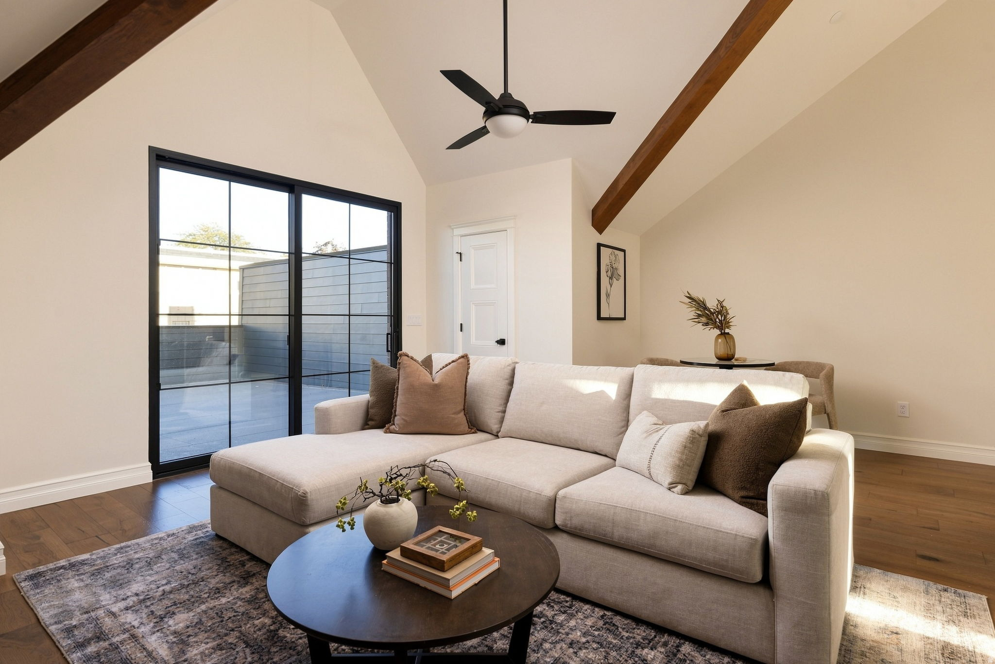 Vaulted ceiling with exposed wood beams, wood-finish flooring, and a black-framed sliding glass door